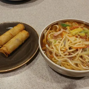 a bowl of noodles and a plate of spring rolls