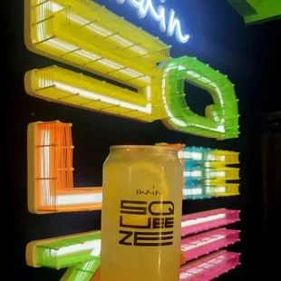 a person holding a can of beer in front of a neon sign