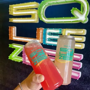 a person holding a drink in front of a neon sign