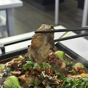 a person holding chopsticks over a dish of food