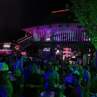 a crowd of people sitting at tables in front of a neon lit building