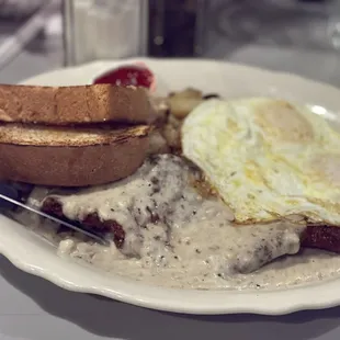 Chicken friend steak and eggs with fresh bread and potatoes.