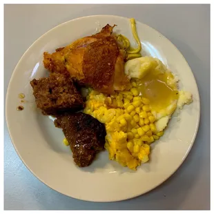 a plate of food with meat, mashed potatoes, corn and gravy