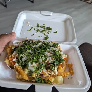 a hand holding a takeout container filled with nachos