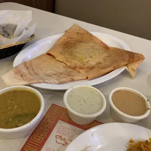 Mysore masala dosa, lentil soup, coconut chutney, and peanut chutney. With paratha in the background.