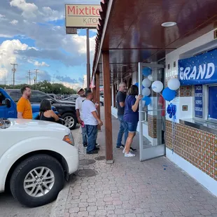 a group of people standing outside of a grand opening
