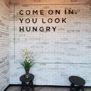 a white brick wall with a sign that says come on in you look hungry