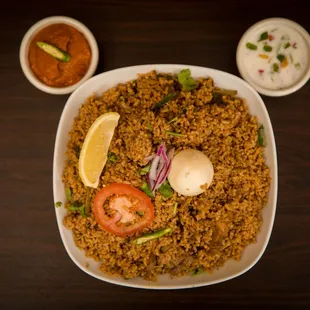 a plate of fried rice with tomatoes, onions, and lemon wedges