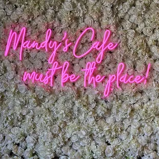 a neon sign in front of a wall of flowers