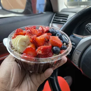 a hand holding a bowl of fruit