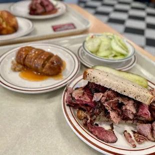 Pastrami on rye, cucumber salad, kishka. Beef knish on the background.