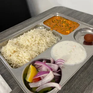 a tray of food with rice, vegetables, and sauces