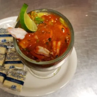 a bowl of soup with shrimp, tortillas, and lime wedges