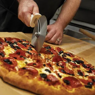 a man slicing a pepperoni pizza