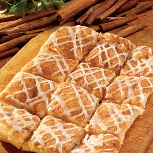 a wooden cutting board with cinnamon rolls and cinnamon sticks