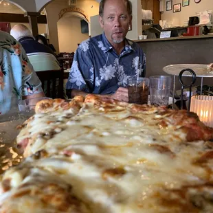 a man sitting in front of a large pizza