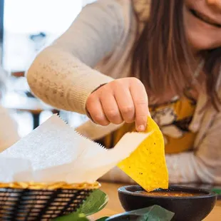 a woman dipping a tortilla into a bowl