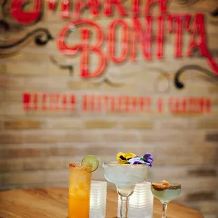 three cocktails on a table in front of a brick wall