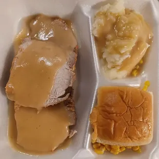 Pork loin in gravy with mashed potatoes and corn and a roll