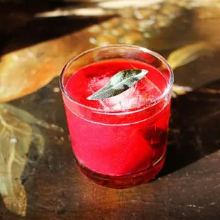 a red drink with a sage leaf garnish