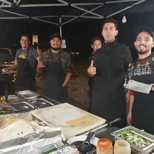 a group of men standing in front of a table of food