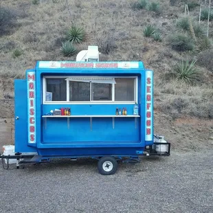 a blue food truck parked in front of a hill