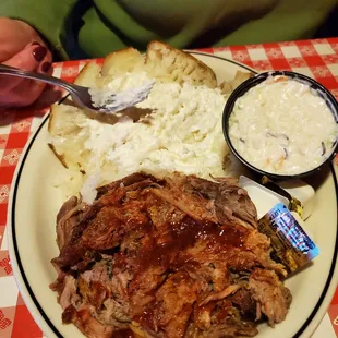 BBQ chopped pork sandwich with baked potato and cole slaw.