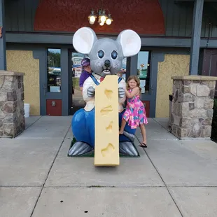 a little girl standing next to a statue of a mouse holding a piece of cheese