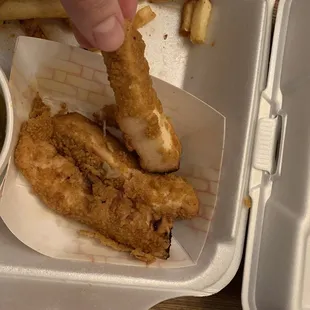 a hand picking a piece of fried chicken