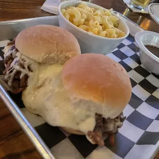 a tray of pulled pork sandwiches with macaroni and cheese