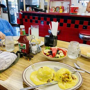Crab Cakes Benedict, Bowl of Fresh Fruit, a giant Hot Cake and Ray's Country Fried Steak &amp; Eggs is behind the mug.