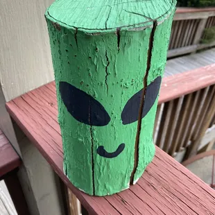a green alien face painted on a piece of wood