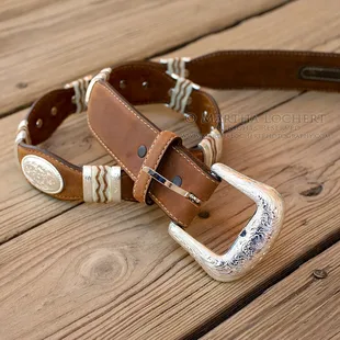 Product photography of a western-style leather and silver belt sitting on a boardwalk