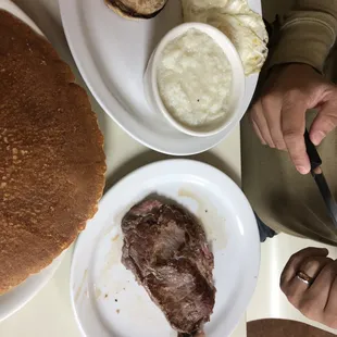Steak and eggs platter with English muffin and grits. With side of banana pancakes