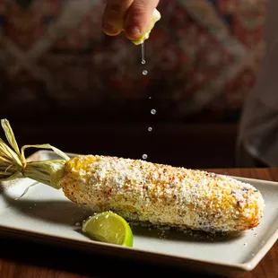 a person sprinkling salt on a corn cob