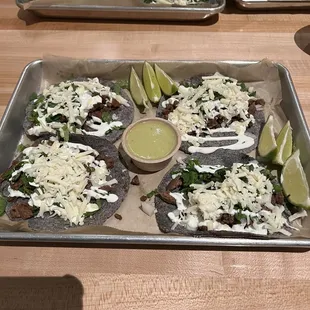 a tray of tacos with lime wedges