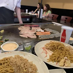 Hibachi chef grilling chicken, steak, shrimp, salmon, and scallops.