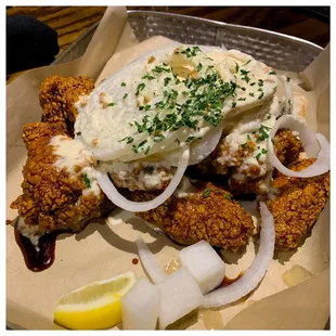 a plate of mashed fried chicken with onions and a lemon wedge