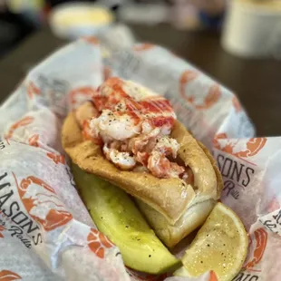 a lobster roll with a pickle and a slice of lemon