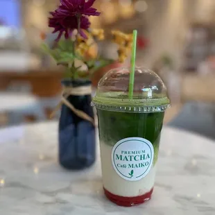 a cup of matcha with a straw and a flower in a vase