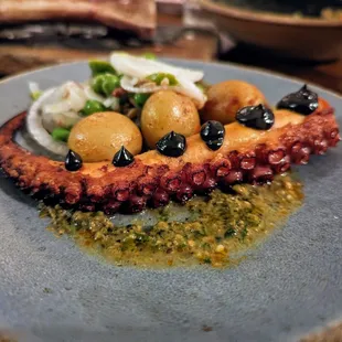 Pulpo a la Plancha. $16. Octopus, romesco verde, new potatoes, black garlic aioli, spring vegetables.