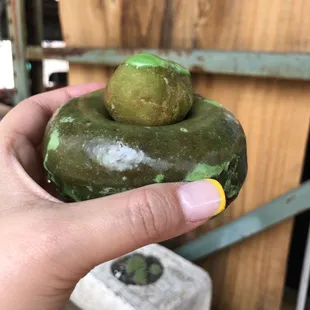 a hand holding a donut with green icing