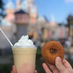 a hand holding a donut and a drink