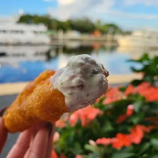 a hand holding a donut covered in cream