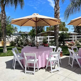 Round table with umbrella, white wooden chair and pink cloths.
