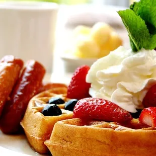 a plate of waffles with strawberries, blueberries, and whipped cream