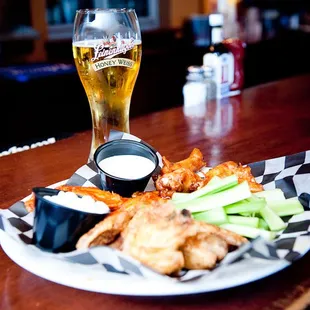 a plate of chicken wings, celery, and a glass of beer
