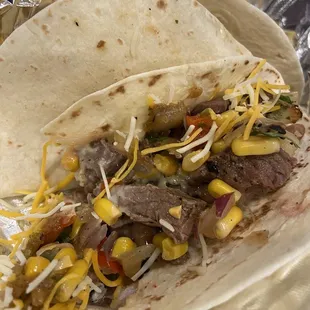 Steak tacos with corn salsa, queso and shredded cheese.