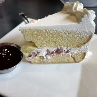 Tres leches cake with fresh strawberries and whipped cream served with side of raspberry sauce