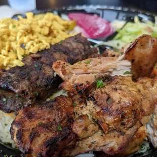 Combo Lunch Special, chicken shwarma, beef kabob, chicken kabab on rice with some onions and salad in the background.